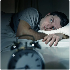 Man lying awake in bed at night, staring at the ceiling, with an alarm clock in the foreground, illustrating difficulty sleeping.