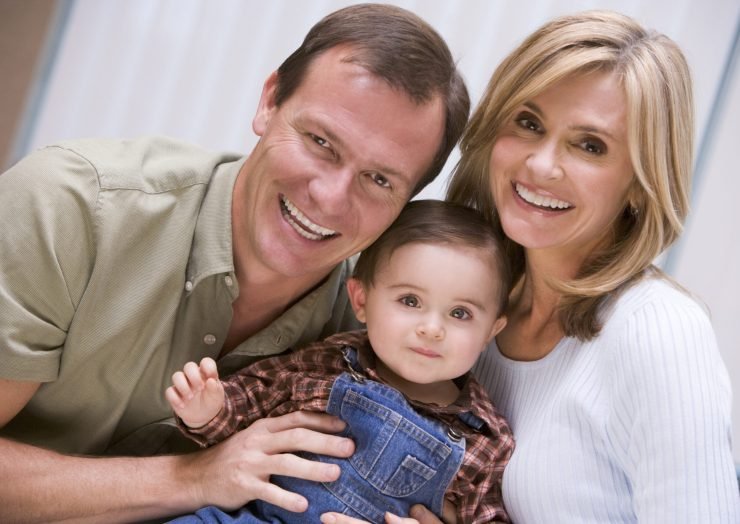 Young parents sitting close together, holding their toddler in a family portrait